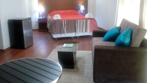 A hotel room with a bed, a sofa, a coffee table, a TV, and a speaker.