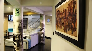A hallway with a staircase, a framed abstract painting, and two pillars with a 'S' sign.