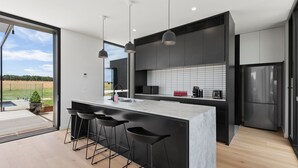 Una cocina moderna con una isla grande, taburetes negros y vistas al exterior.