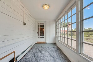 Un couloir aux murs en bois peints en blanc, un tapis gris et une grande fenêtre donnant sur l’extérieur.