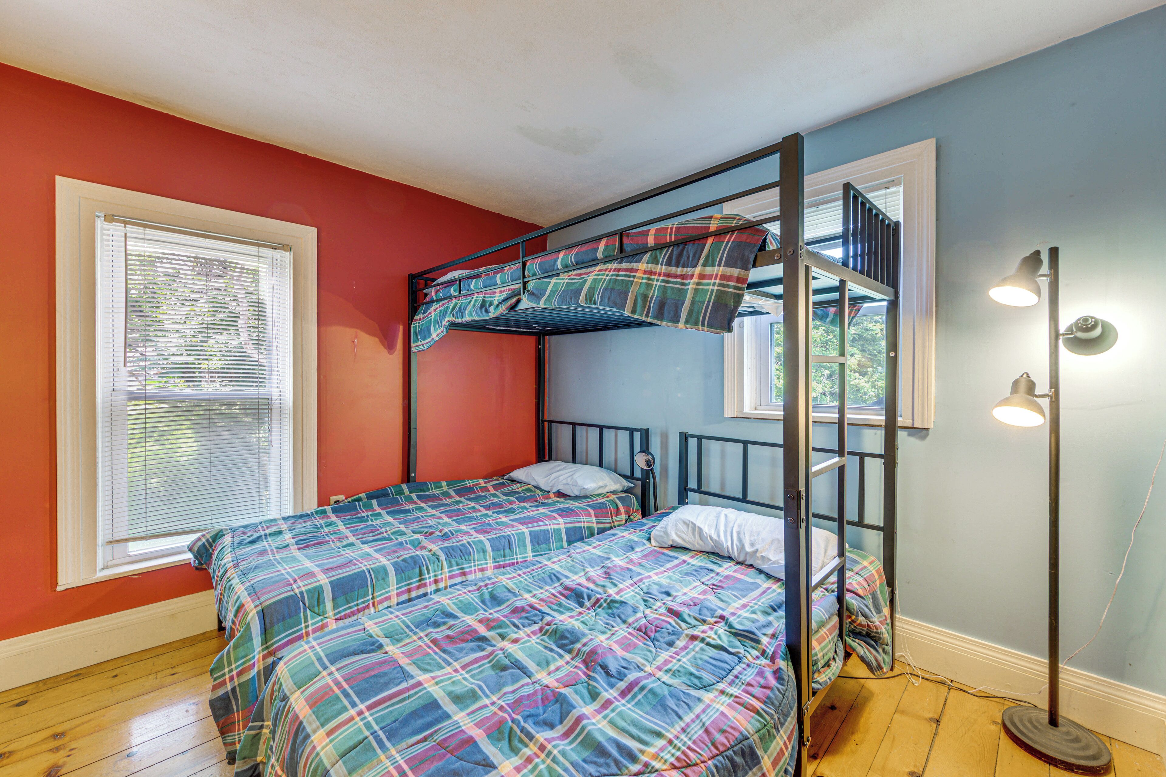Ein Stockbett mit Karoüberwurf, ein Fenster mit Jalousien und eine Stehlampe.