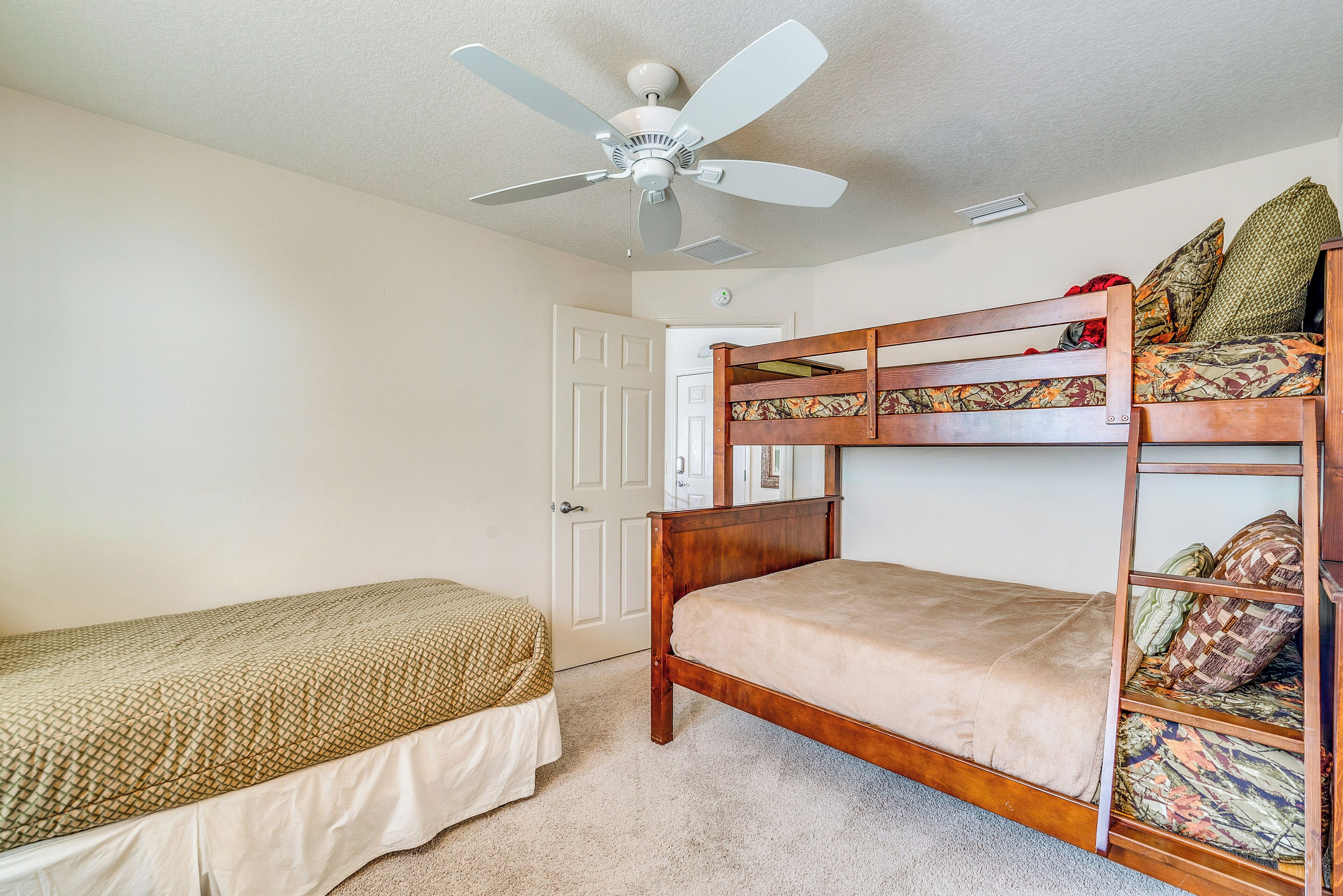A bedroom with a bunk bed, a single bed, a ceiling fan, and a door.