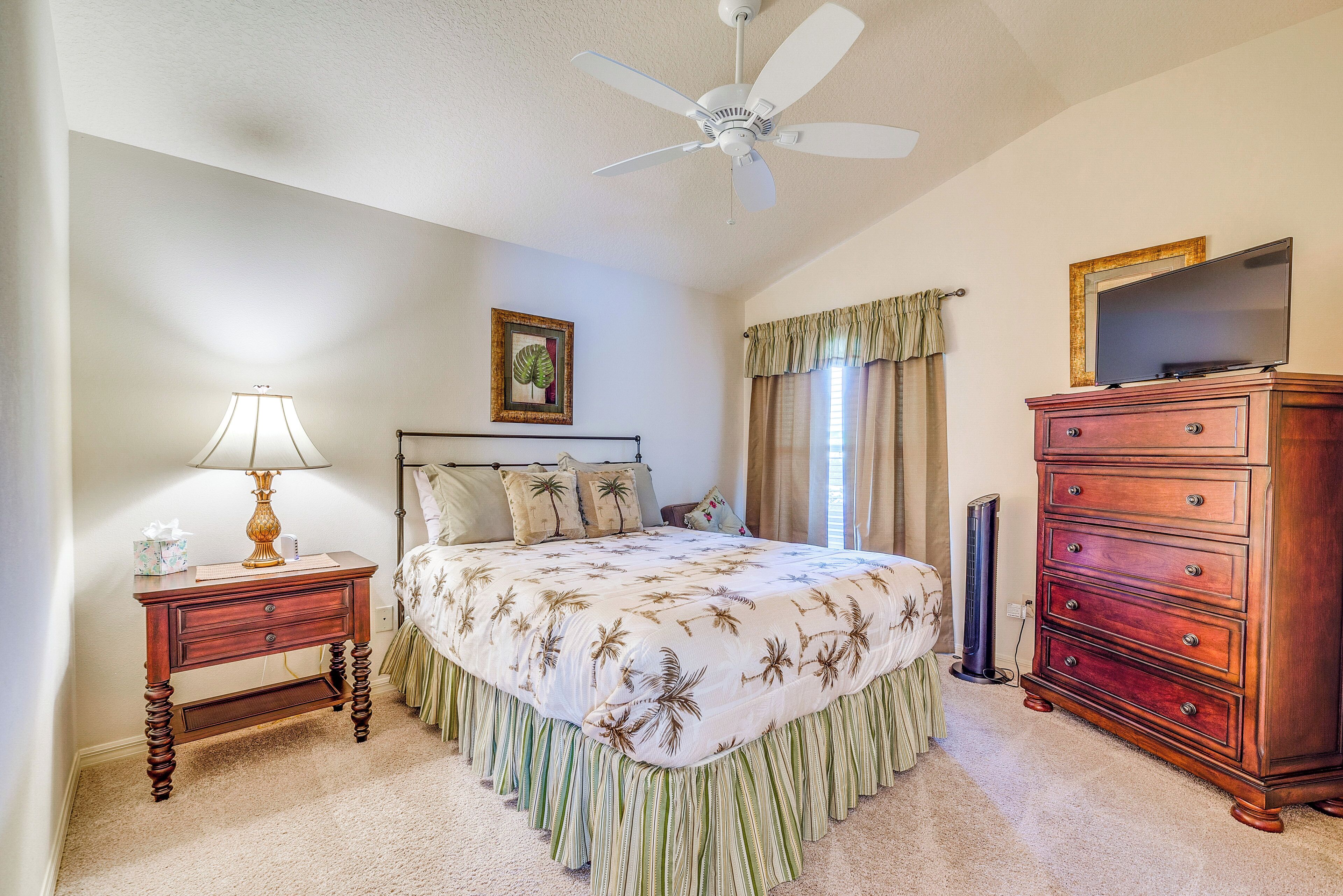 A bedroom with a bed, a dresser, a nightstand, a lamp, a ceiling fan, and a television on a dresser.