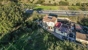 An aerial view of a rural area with a house, a road, and surrounding vegetation.