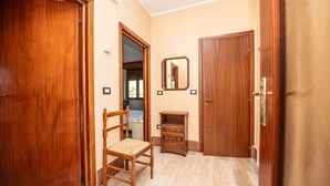 A hallway with wooden doors, a wooden chair, a small wooden cabinet, and a mirror on the wall.