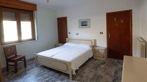 A bedroom with a bed, wooden wardrobe, a chair, a small bedside table, and a radiator.