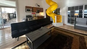 A modern living room with a black sofa, a wooden coffee table, and a yellow spiral staircase leading to a balcony. - Experience Scottsbluff charm in our spacious 4-bedroom retreat (Scottsbluff)