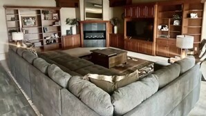 A spacious living room with a large sectional sofa, a flat-screen TV, wooden cabinets, and a fireplace. - Experience Scottsbluff charm in our spacious 4-bedroom retreat (Scottsbluff)
