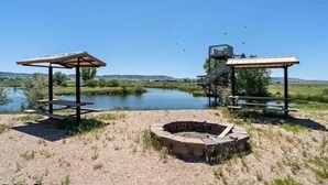 A lakeside outdoor area with picnic tables and a fire pit. - Experience Scottsbluff charm in our spacious 4-bedroom retreat (Scottsbluff)