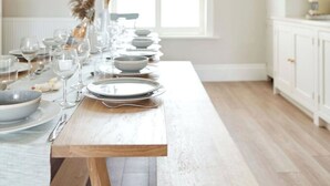 Un comedor con una larga mesa de madera preparada para una comida, una lámpara colgante y una ventana que proporciona luz natural.