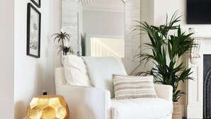 Un sillón blanco con reposapiés de estampado geométrico, un espejo grande y una planta en maceta en un salón moderno.