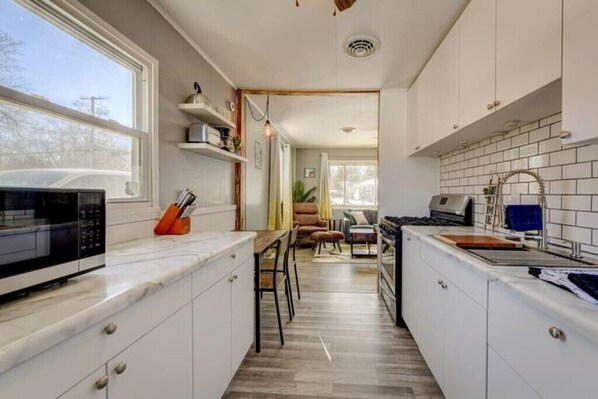 A compact kitchen with white cabinets, a microwave, and a sink. There is a dining area with a table and chairs in the background.