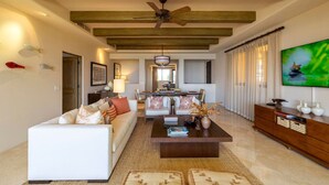 A spacious living room with a high ceiling, a ceiling fan, a large flat-screen TV, and a dining area with a chandelier. - Hacienda Beach Club, Beachfront, 5-Star, Luxury (Cabo San Lucas)