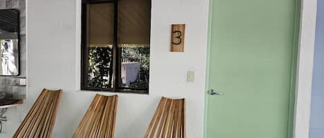 Una habitación con tres sillas de madera, una puerta verde y una ventana que da a zonas verdes.