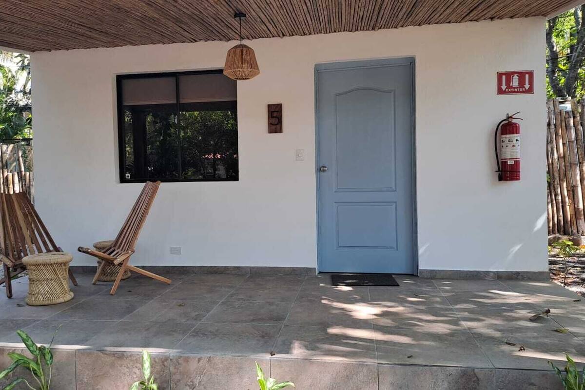 A covered outdoor area with a blue door, a fire extinguisher, and two wooden chairs.