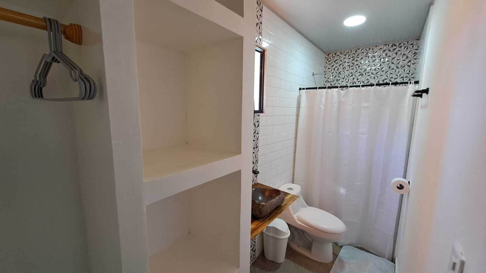 Un baño con inodoro, un lavabo de piedra, cortina de ducha y un perchero para toallas.