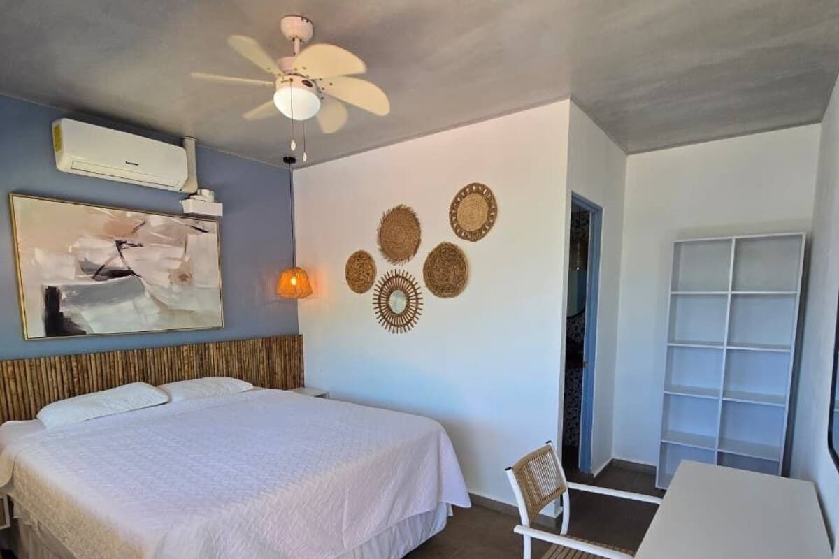 A bedroom with a bed, a desk, a chair, a ceiling fan, wall decor, and an air conditioning unit.