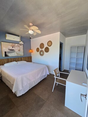 A bedroom with a bed, a desk, a chair, a ceiling fan, wall decor, and an air conditioning unit. - Hotel Zelen (Tamanique)
