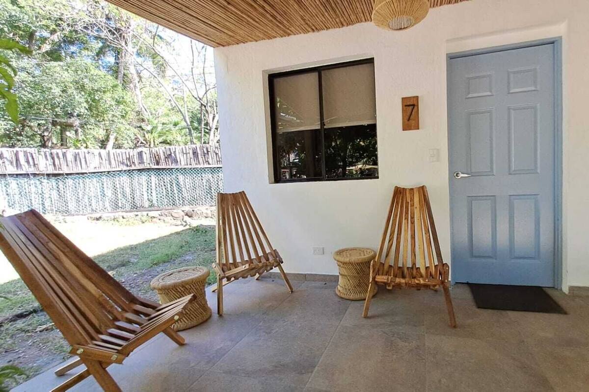A room with three wooden chairs, a window, a blue door, and a fire extinguisher on the wall.