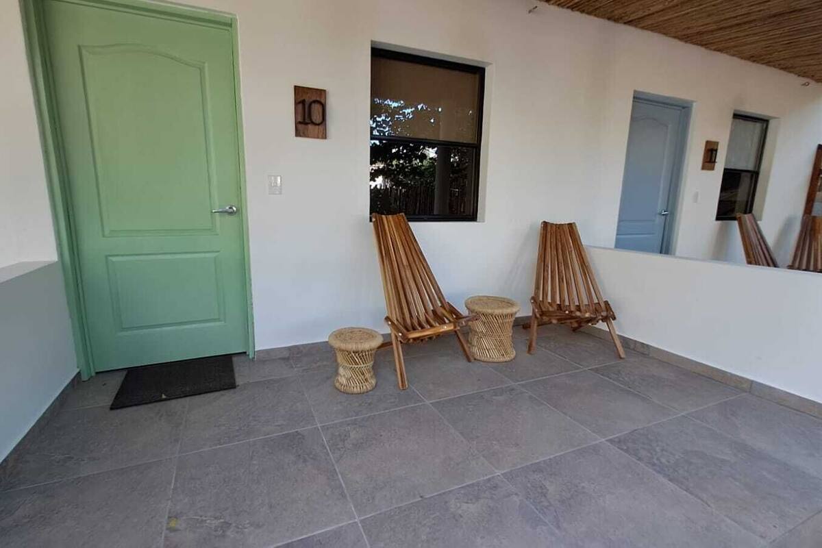 A room with a green door, a window, and two wooden chairs with stools.