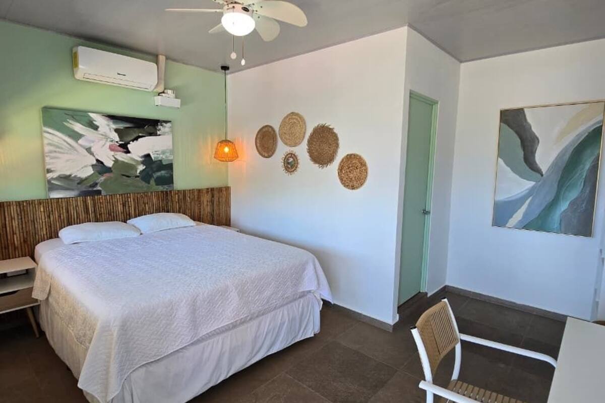 A bedroom with a bed, a ceiling fan, a chair, and artwork on the walls.