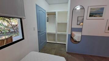 Un dormitorio con ventana, puerta, armario y espejo.