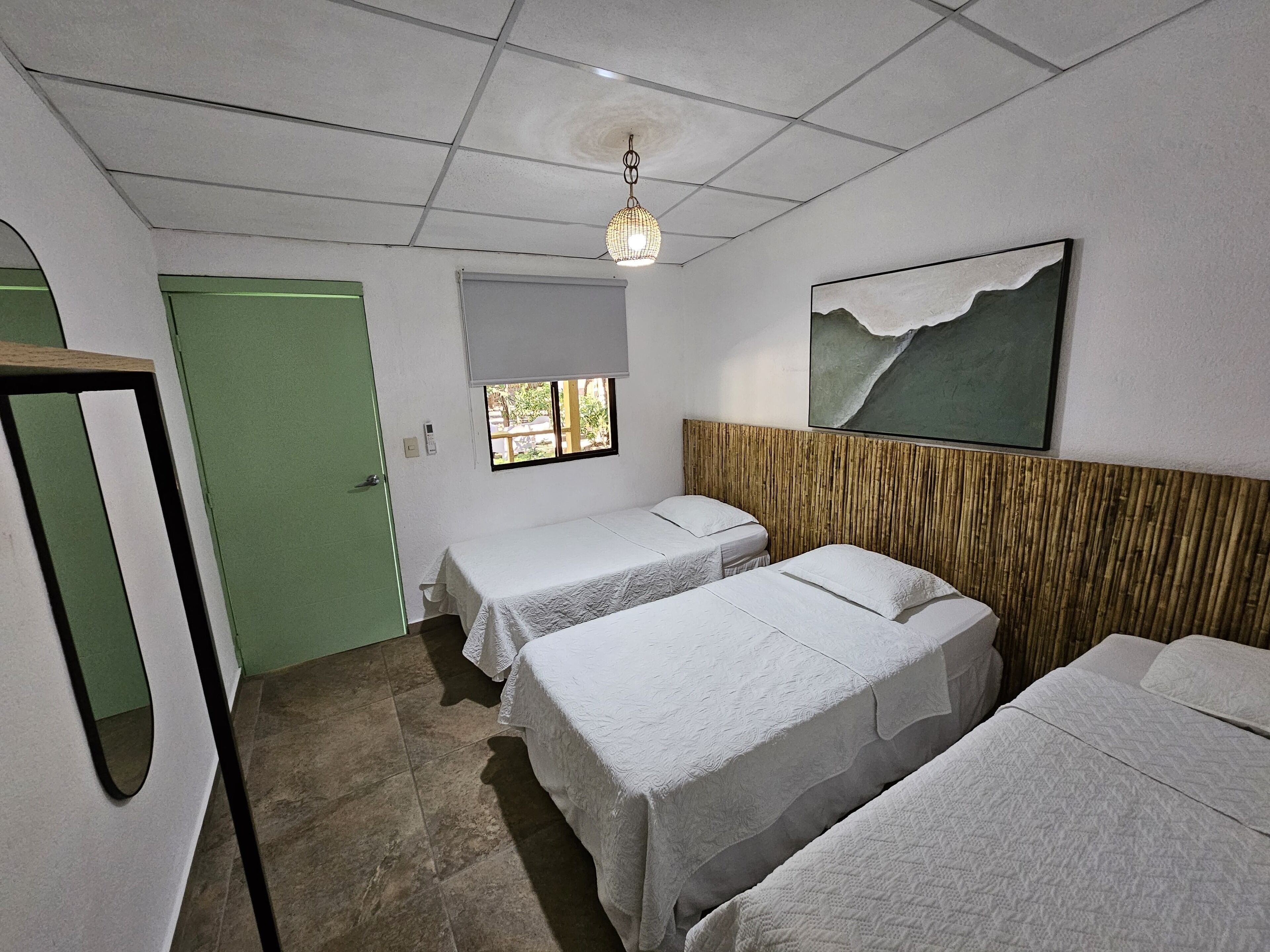 Une chambre d’hôtel avec deux lits simples, une fenêtre donnant sur un paysage agréable, un tableau au mur et un luminaire au plafond.