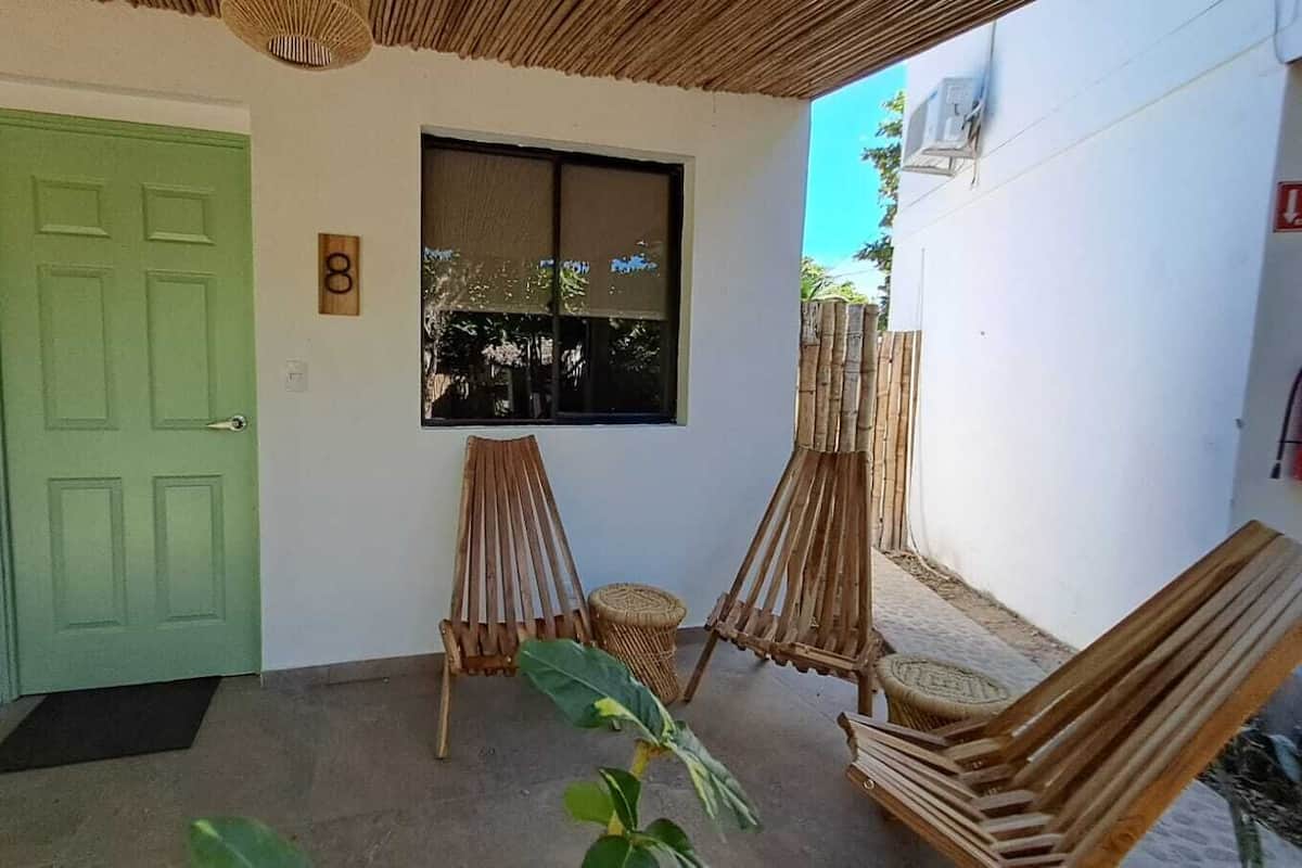 A green door, a window, and a small room with two wooden chairs and a table.