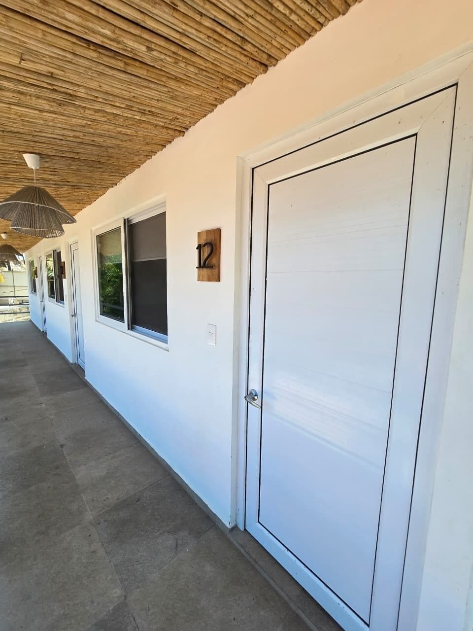 A corridor with a wooden ceiling, a closed door, and a window with a number plate.