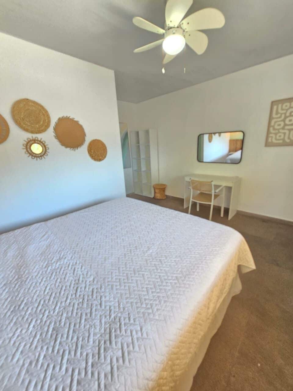 Un dormitorio con cama, ventilador de techo, escritorio y una silla.