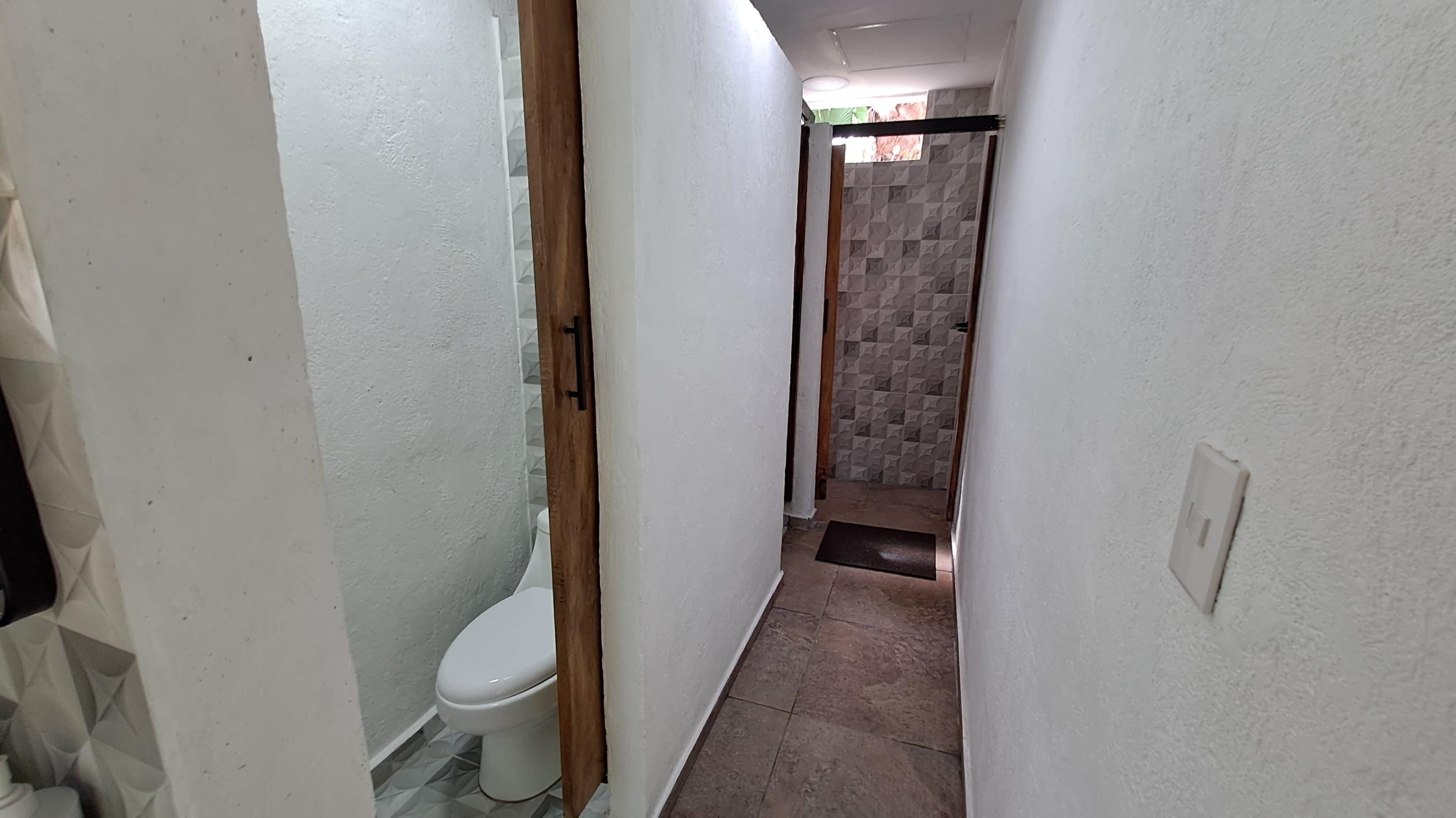 En smal gang med toilet på venstre side og et bruseområde med væg i geometrisk mønster på højre side.