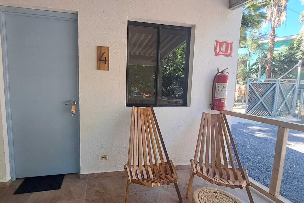 A door with a number '4' sign, two wooden chairs, a window, and a fire extinguisher.