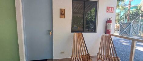 Una puerta con un cartel con el número 4, dos sillas de madera, una ventana y un extintor.