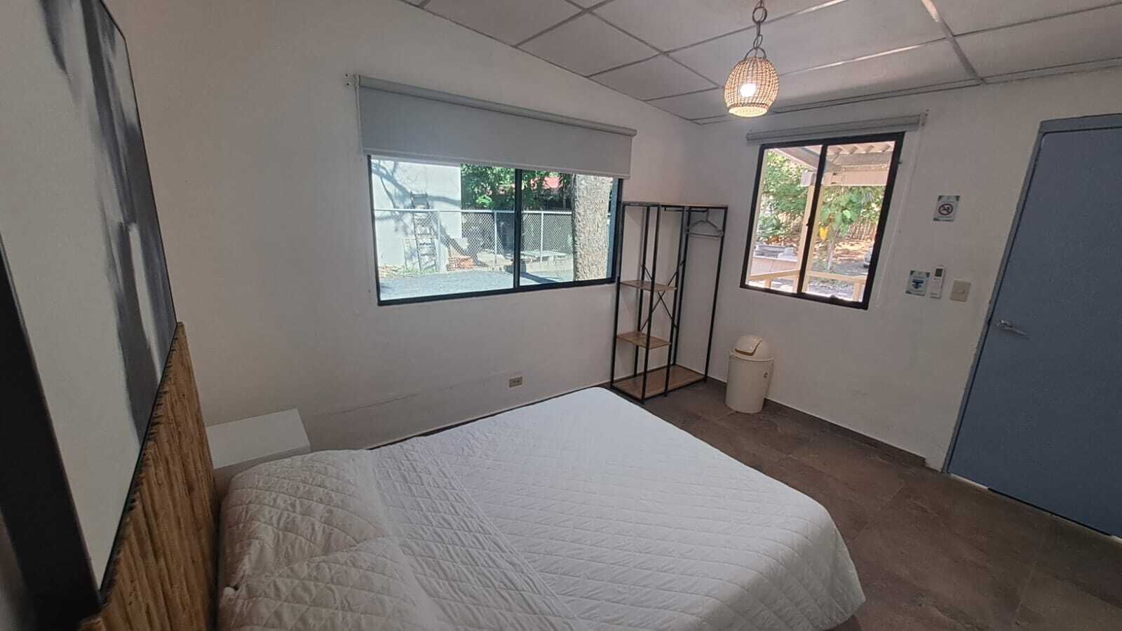 A bedroom with a bed, a window, a door, and a hanging light fixture.
