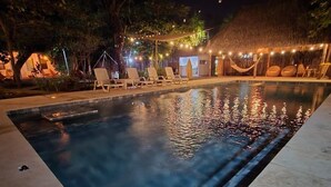 Ein Schwimmbecken bei Nacht mit Liegestühlen und Lichterketten.