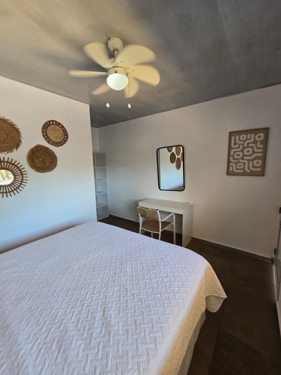 A bedroom with a bed, a desk, a chair, a ceiling fan, and wall decorations.