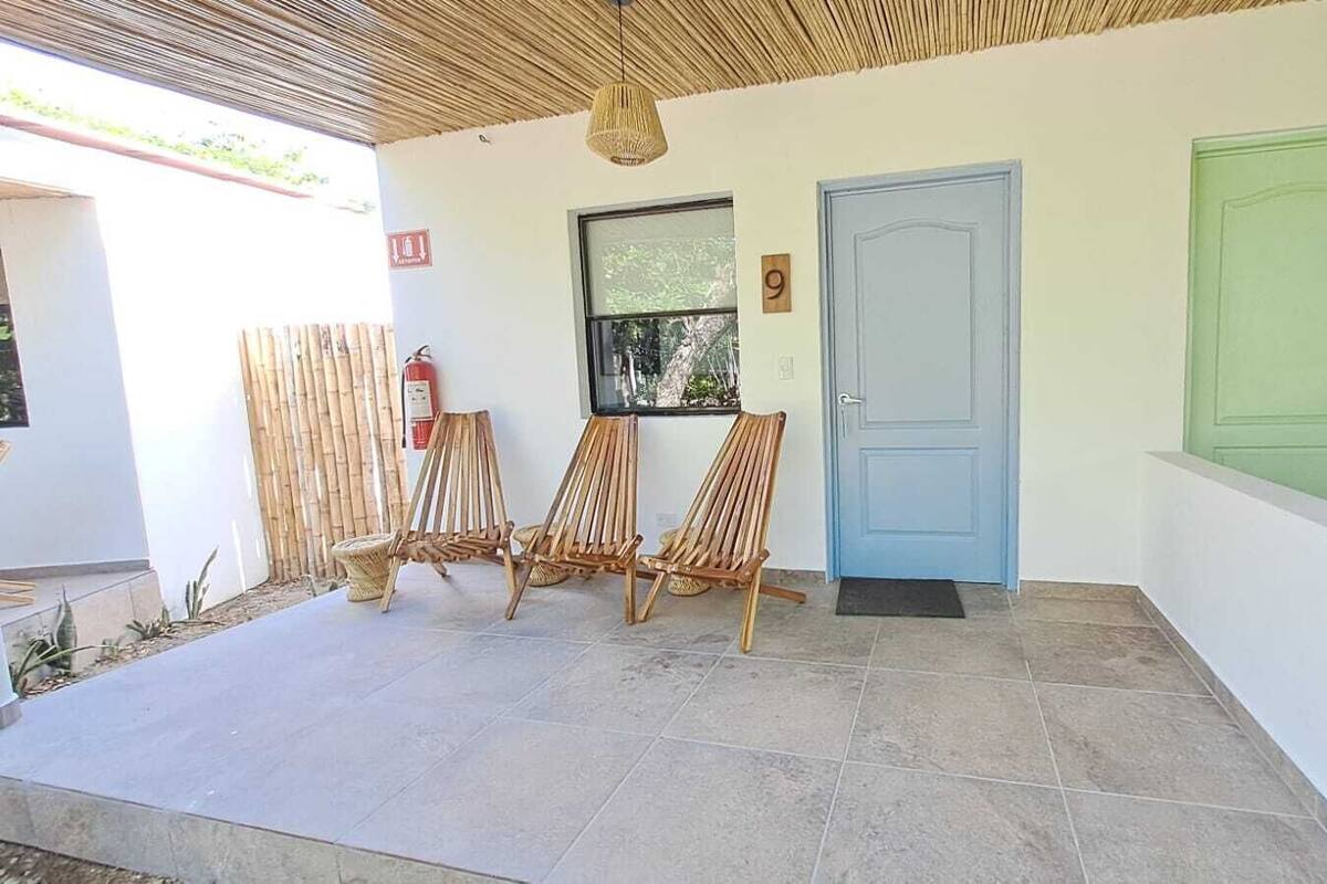 A covered outdoor area with three wooden chairs, a blue door, and a green door.