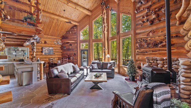 Ein rustikaler Innenraum einer Blockhütte mit Kamin aus Stein, Ledersofas und Steinböden.