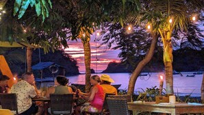 A group of people dining at an outdoor restaurant with a view of the sunset over water.