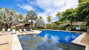 Une piscine avec des chaises longues, des palmiers et un bâtiment doté d’un toit en tuiles.