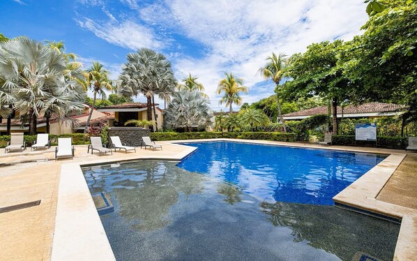 A swimming pool with lounge chairs, palm trees, and a building with a tiled roof.