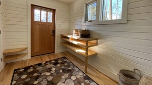 A room with a wooden door, a window with a view of trees, a shelf with baskets, and a patterned rug. - Aspen House, the "not so tiny" house! (Golden)
