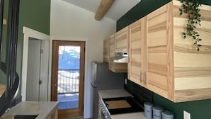 A modern kitchen with wooden cabinets, a marble countertop, and a view to the outside. - Aspen House, the "not so tiny" house! (Golden)