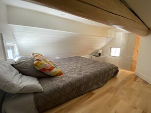 Cozy loft-style bedroom with a large bed, patterned bedspread, and two windows.