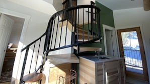 A modern kitchen with a built-in island, a black spiral staircase, and a view of the outdoors. - Aspen House, the "not so tiny" house! (Golden)