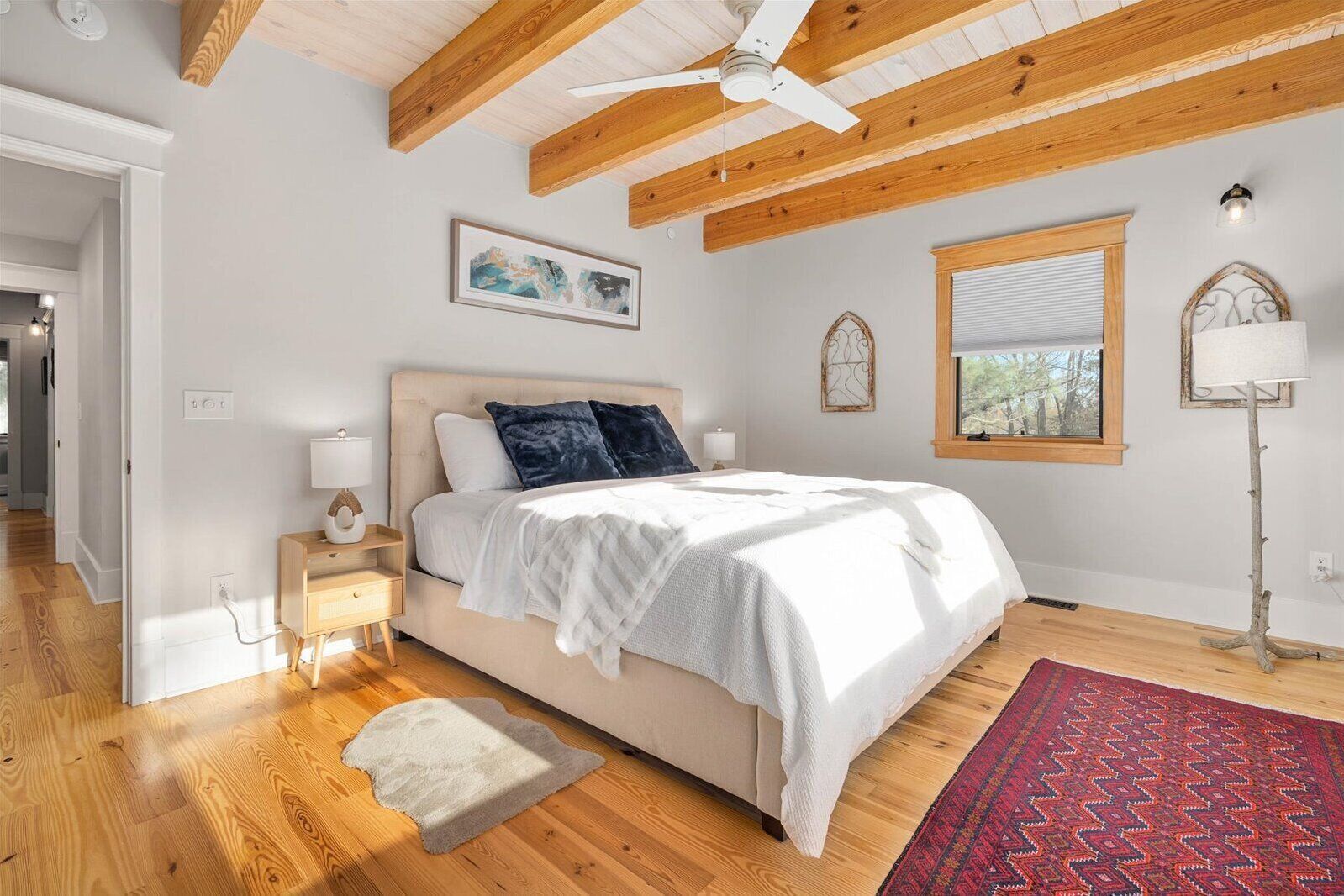 Ein Schlafzimmer mit Bett, Holzboden, Deckenventilator, Kunstwerk, Fenster und einer Lampe.
