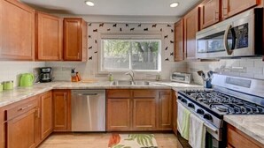 Una cocina con gabinetes de madera, electrodomésticos de acero inoxidable, un ventanal con vistas y un tapete estampado.
