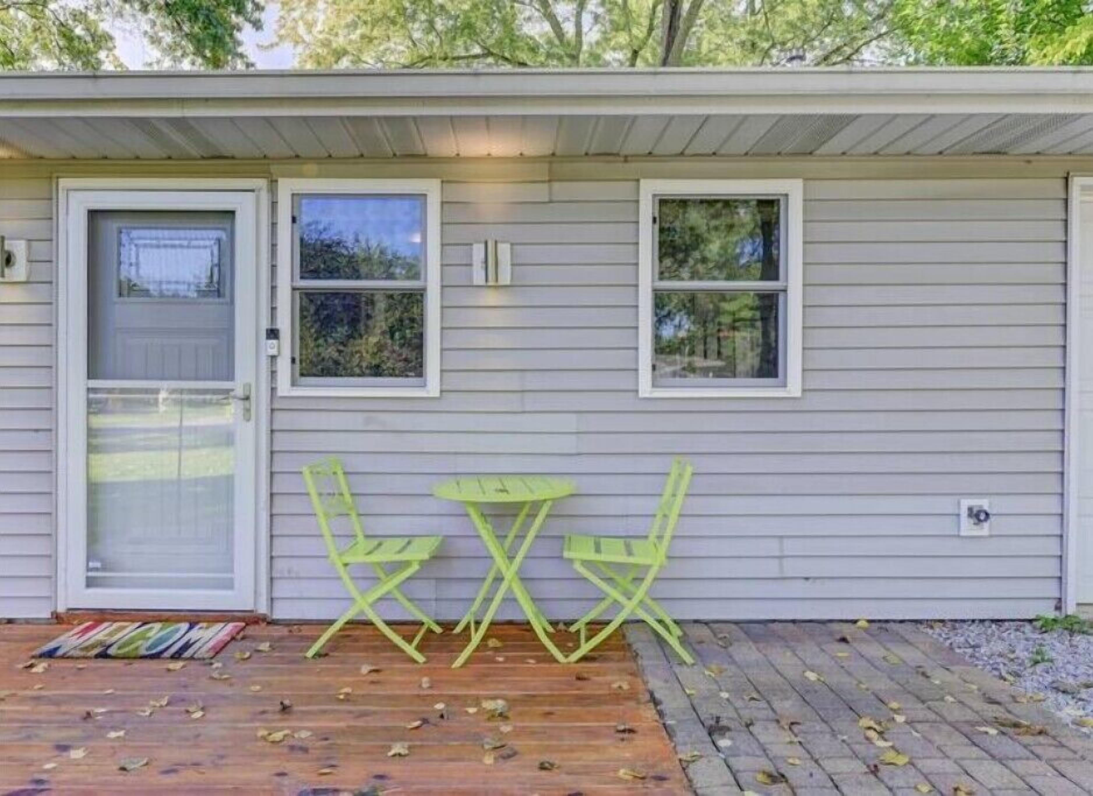 Una casita con terraza de madera, una puerta y dos ventanas.