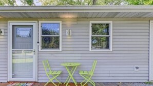 Una casita con terraza de madera, una puerta y dos ventanas.
