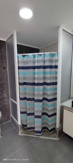 A bathroom with a striped shower curtain, a mirror, and a tiled floor. - Centro de Descanso Los Poetas (El Quisco)